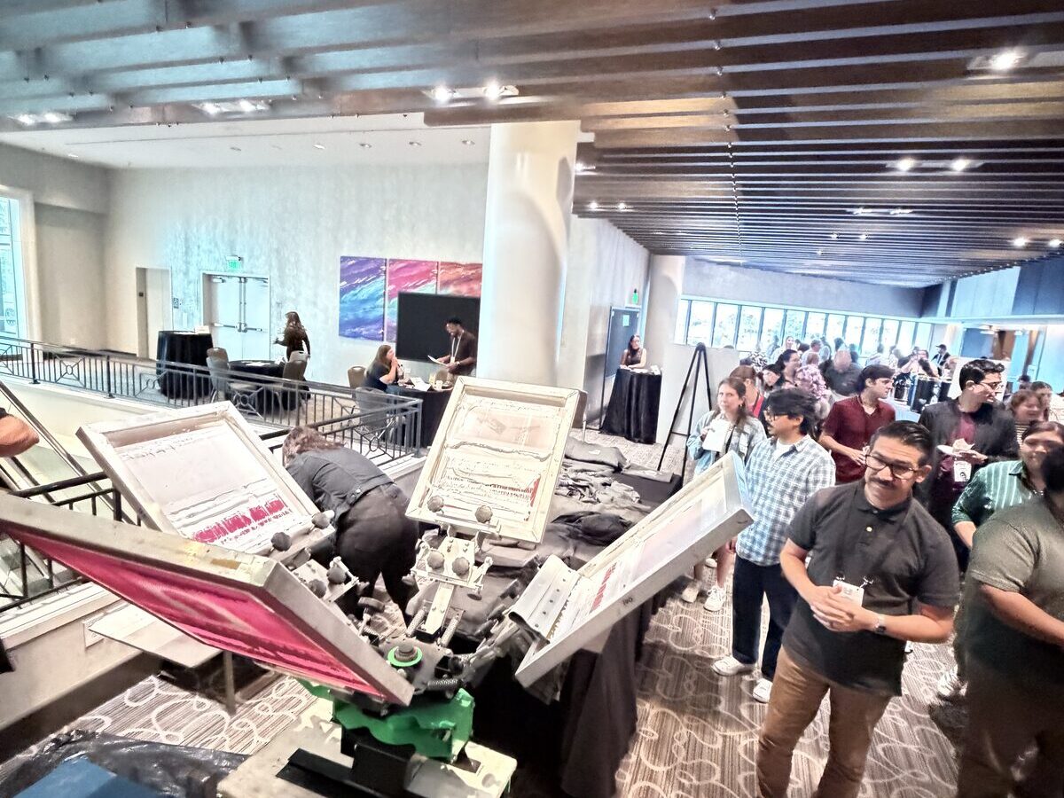 Conference attendees lining up at a live screen printing carousel in a ballroom